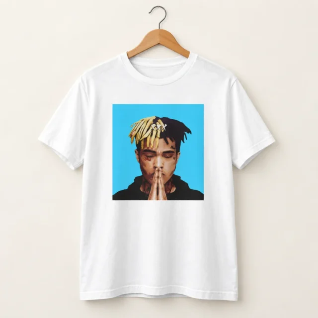 Studio view of a T-shirt with illustrated XXXTentacion portrait on a blue background