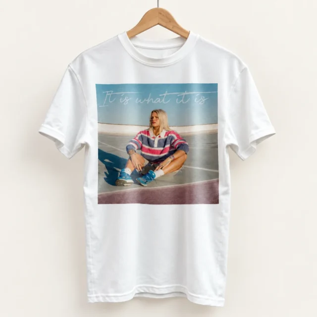 Studio view of a T-shirt with it Is What It Is illustrated quote panel with a seated figure